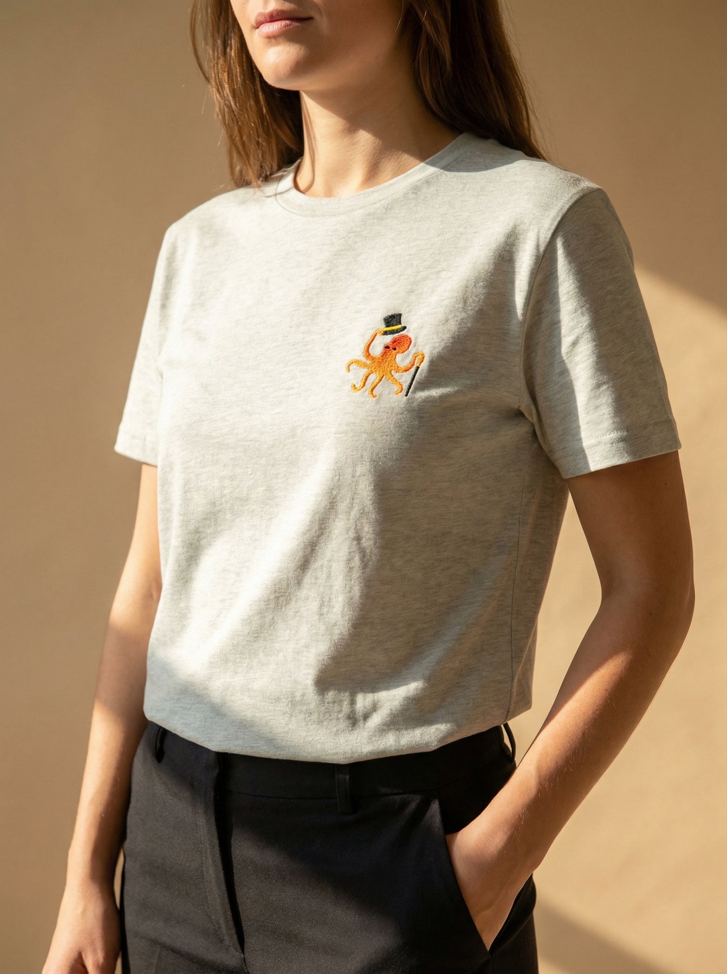 Person wearing a light gray t-shirt with a small embroidered design on a beige background