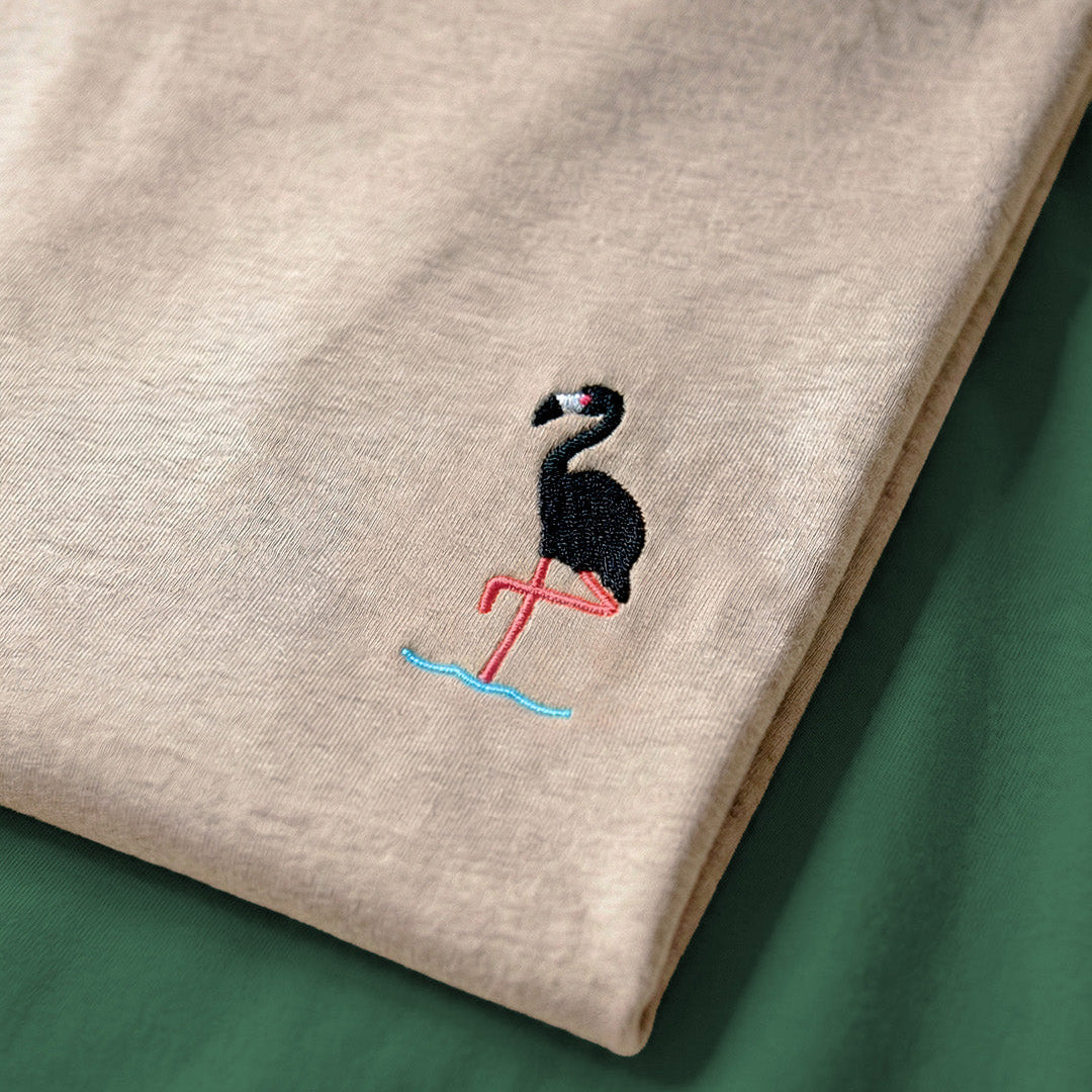 Beige fabric with an embroidered flamingo design on a green background