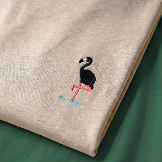 Beige fabric with an embroidered flamingo design on a green background