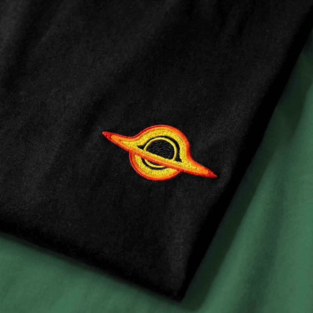 Black t-shirt with a colorful embroidered logo on a green surface