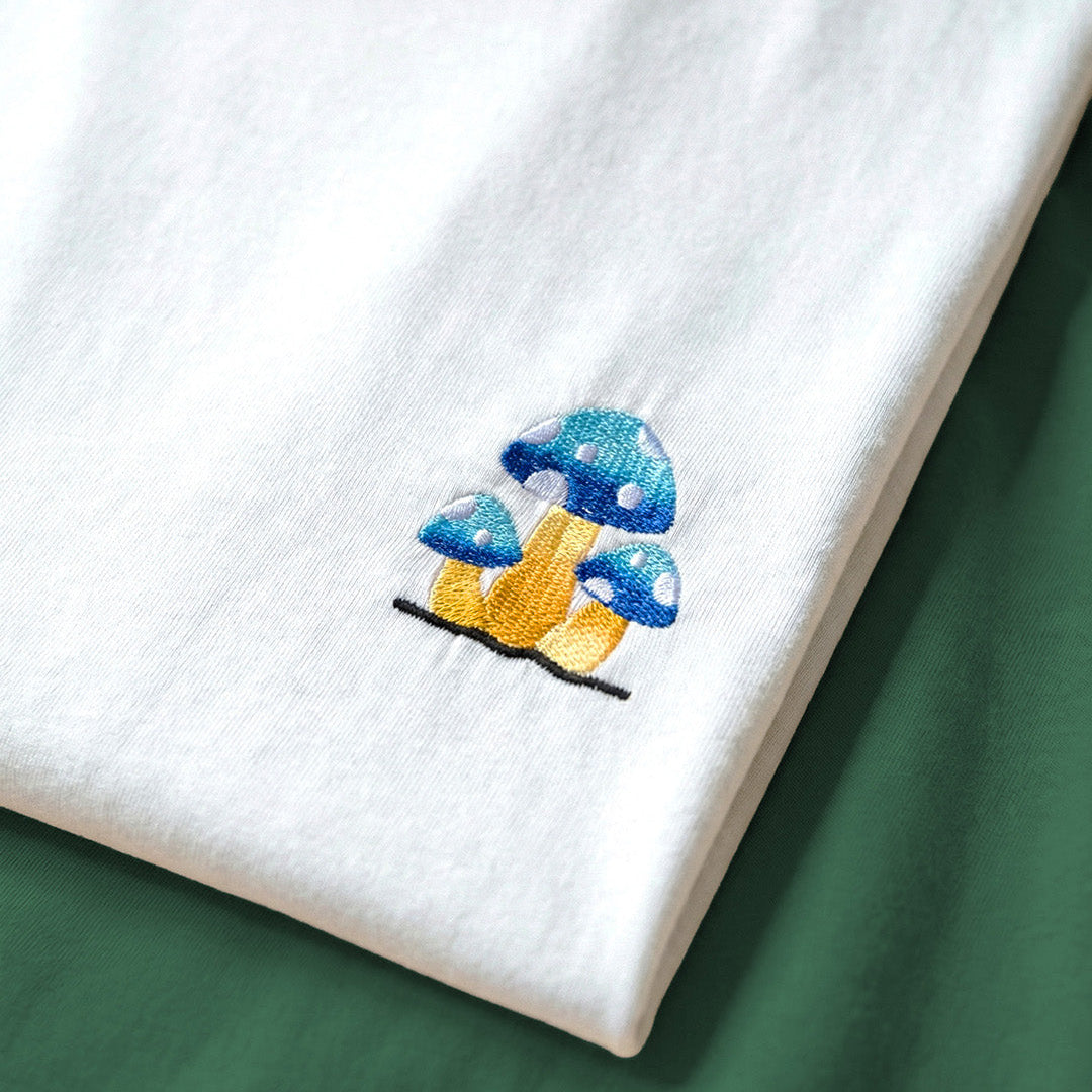 White fabric with embroidered blue and yellow mushroom design on a green background