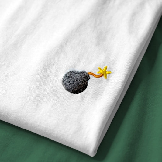 White t-shirt with a small embroidered design of a bomb on a green surface
