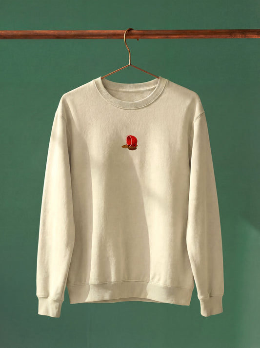 Beige sweatshirt with a small red and yellow design on a hanger against a green background