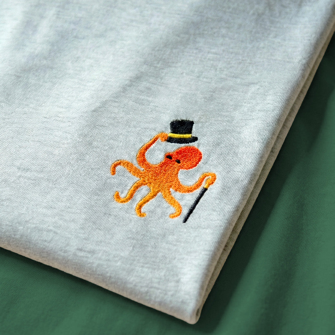 Embroidered orange octopus wearing a black top hat on a gray fabric background