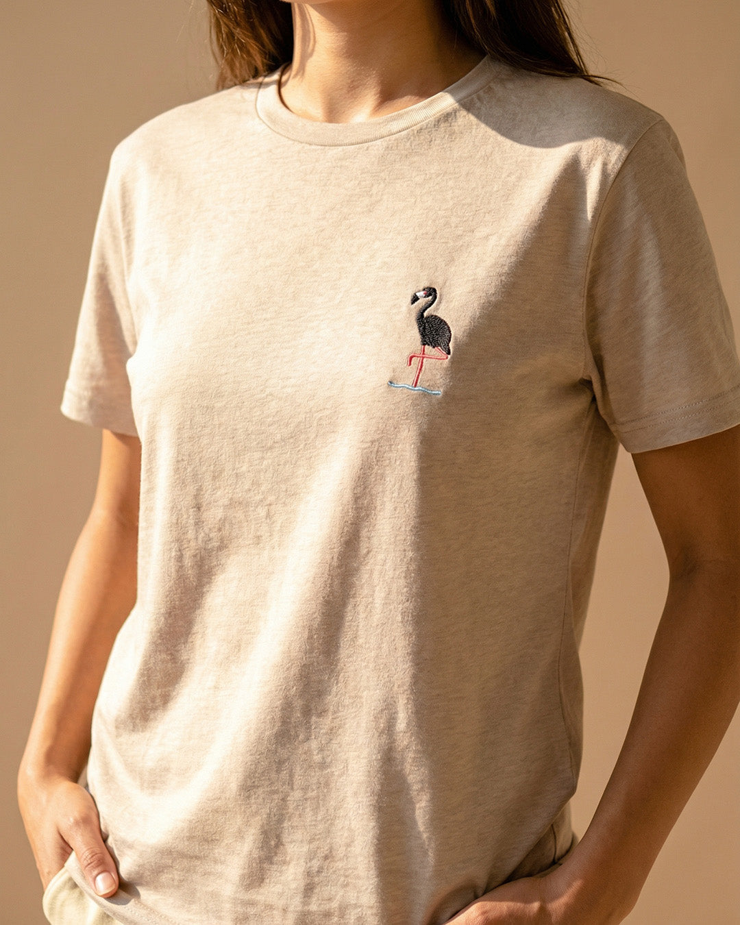 Beige t-shirt with a flamingo graphic worn by a person against a beige background