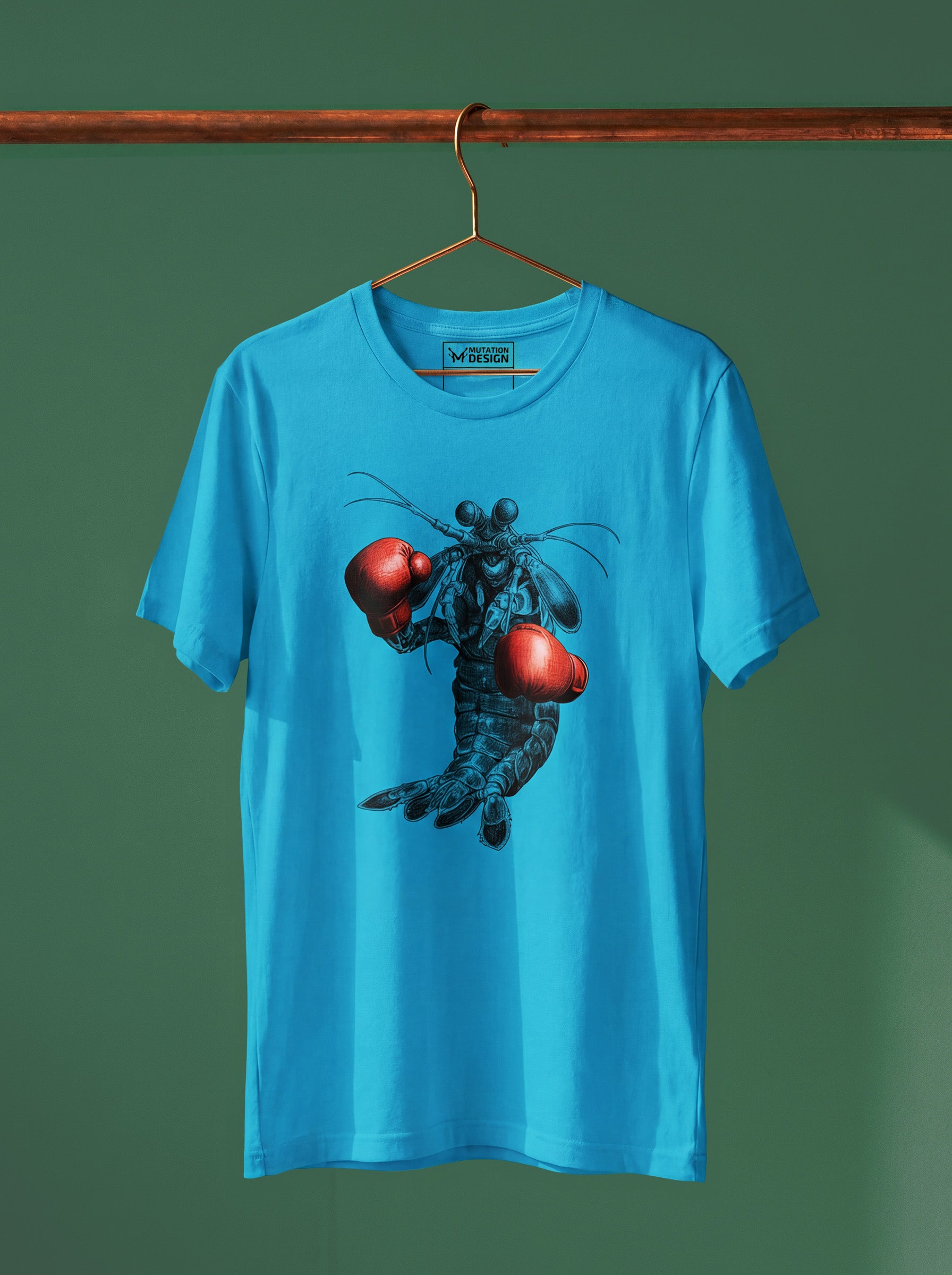 Blue t-shirt with a graphic design of a creature holding red balls on a hanger against a green wall.
