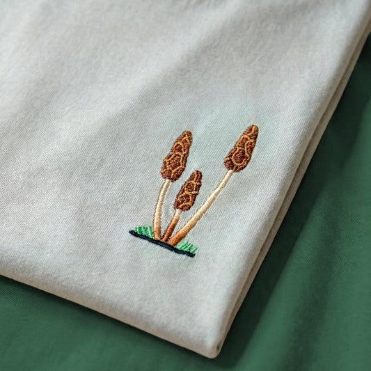 Embroidered design of three mushrooms on a light fabric background