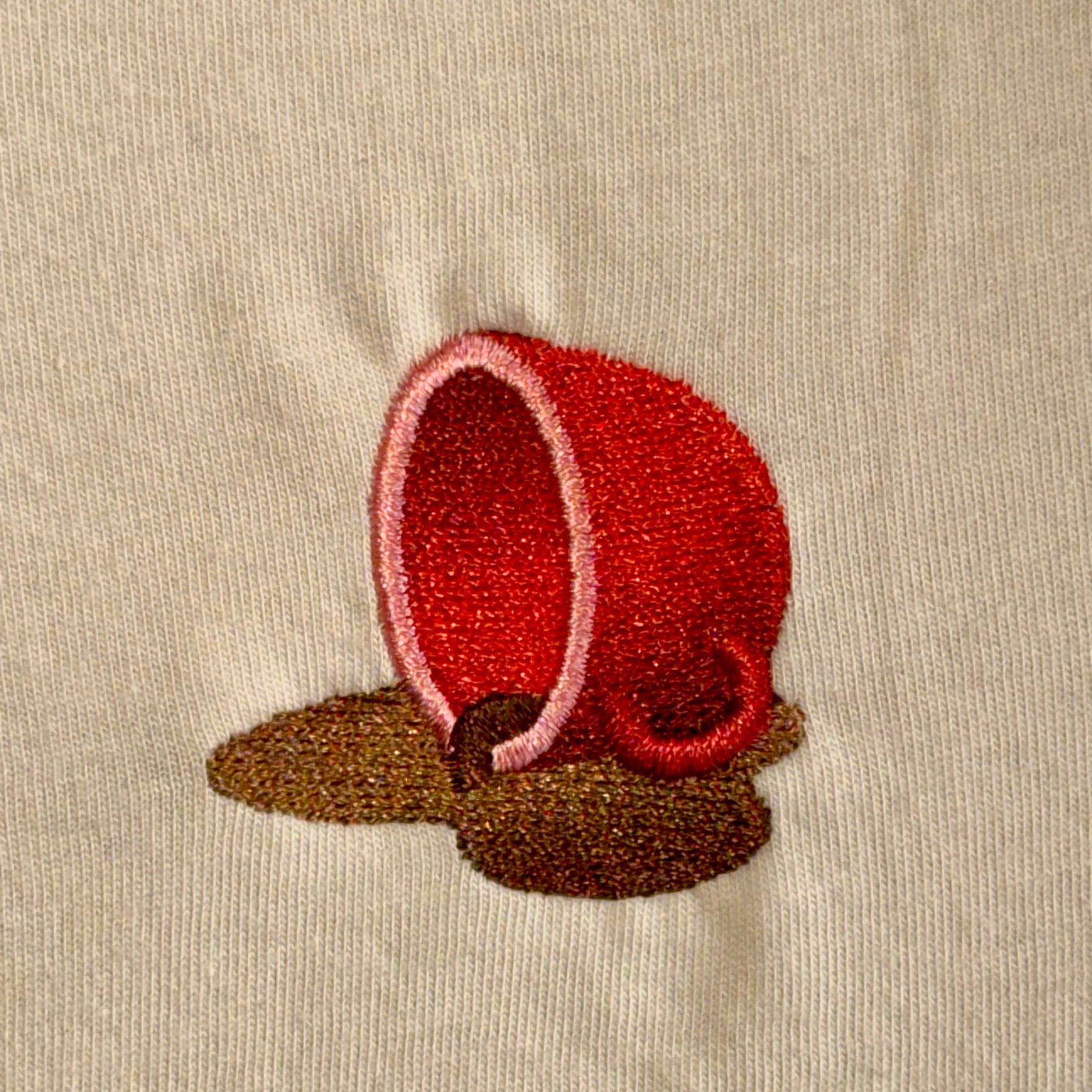 Embroidered red cup with brown base on beige fabric