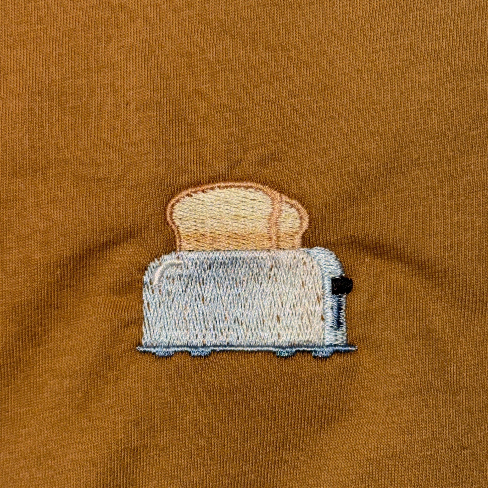 Embroidered toaster with bread on a brown fabric background