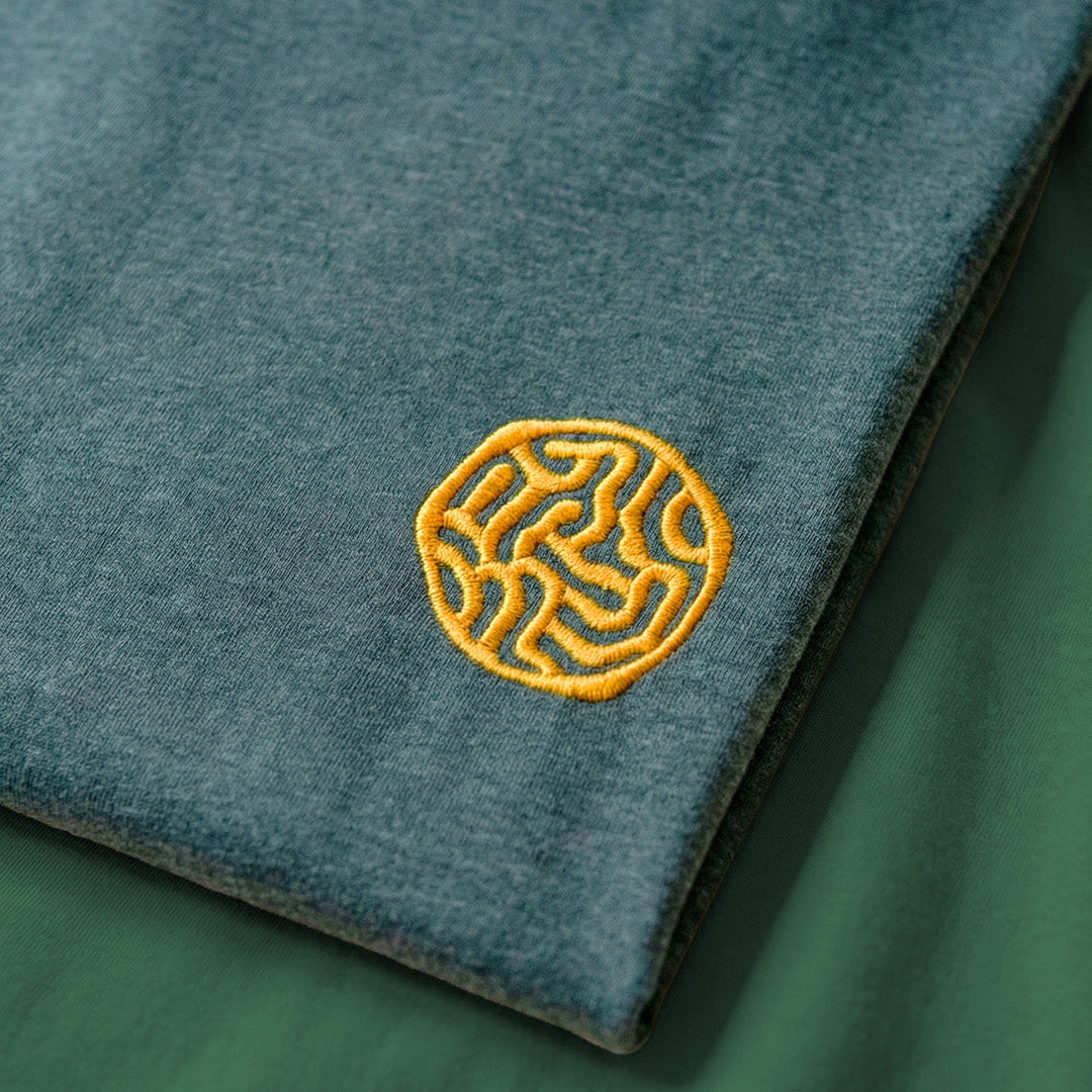 Teal fabric with a yellow embroidered logo on a green background