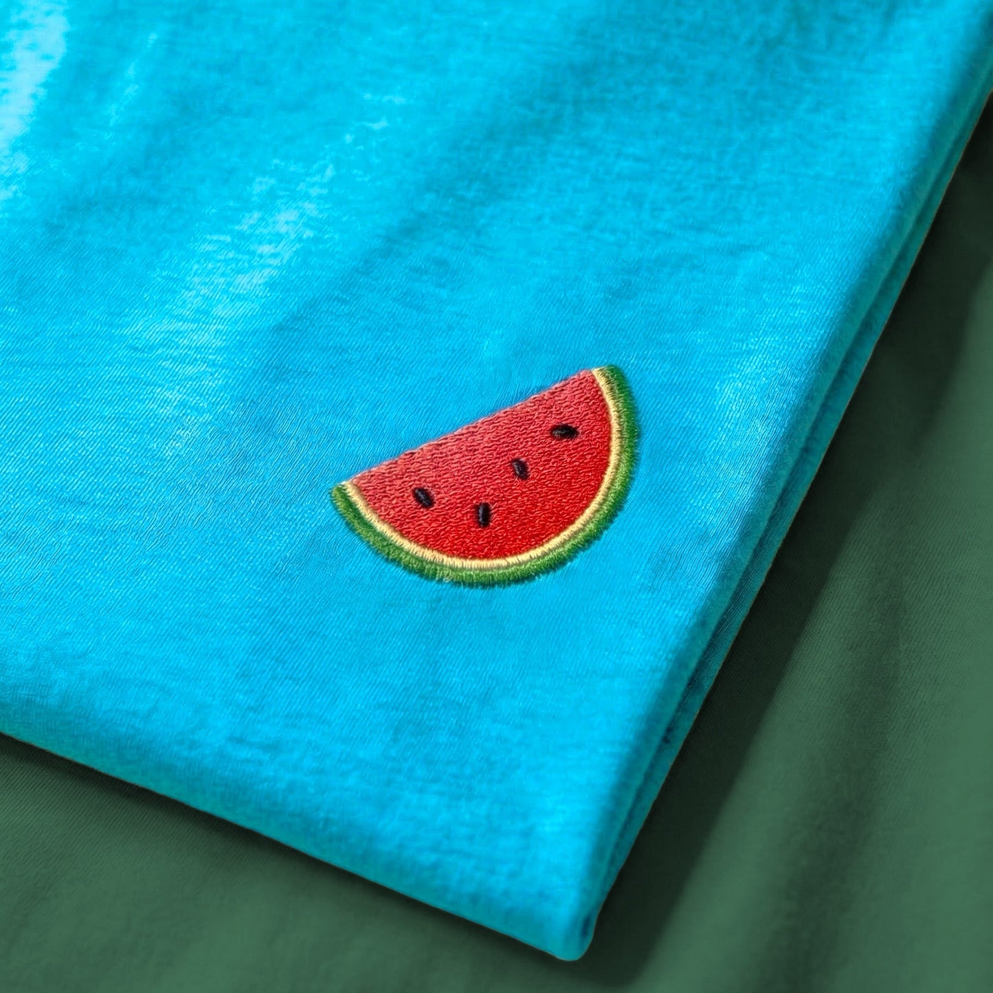 Turquoise shirt with a watermelon slice patch on a green surface
