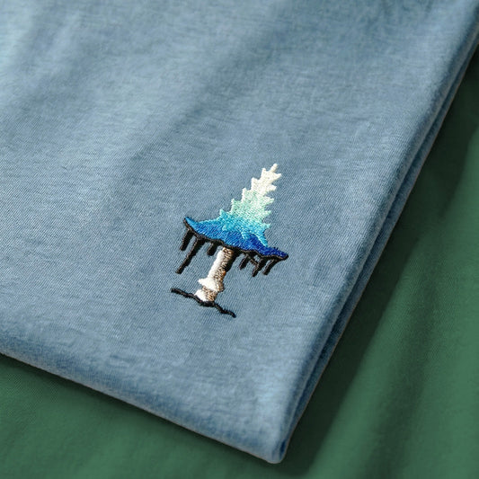 Embroidered design of a blue mushroom on a light blue fabric background